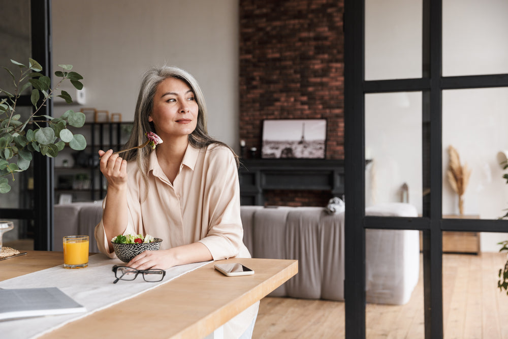 mature amazing woman sitting at kitchen indoors at home while eating salad.
