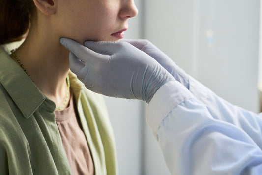 Healthcare professional examining patient's neck with medical gloves inside an examination room during a routine check-up for thyroid and lymph node inspection